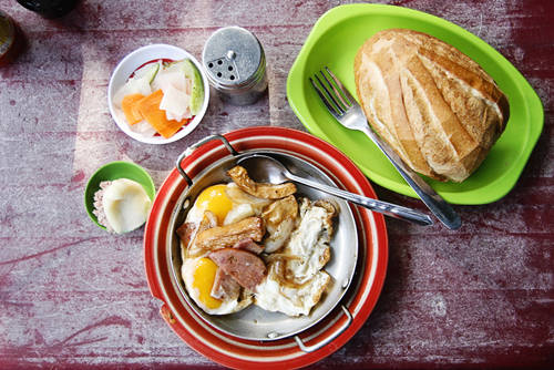 Bánh mì Hòa Mã: Đối với nhiều người, bánh mì là thức ăn nhanh, rất thích hợp đối với cuộc sống tấp nập ở mảnh đất Sài Gòn. Với hương vị khác lạ nhưng không quá đặc biệt, tiệm bánh mì Hòa Mã đã lưu giữ trong mình những kỷ niệm về Sài Gòn từ rất nhiều năm qua. Phần ăn nhiều người hay lựa chọn gồm ổ bánh mì dài khoảng một gang tay, ăn cùng chảo thức ăn nóng hổi, đầy ắp. Bên trong chiếc chảo nhỏ này là đủ thứ nguyên liệu hấp dẫn như trứng gà ốp la, thịt nguội, xúc xích, chả cá, chả lụa,... Tất cả đều được chiên nóng cháy cạnh tỉ mỉ cùng với ít hành tây thái múi cau và dùng nóng với bánh mì. Ảnh: Phong Vinh