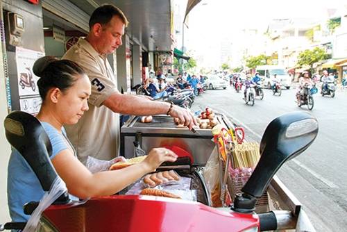 Xúc xích ông Tây Khách quen vẫn thường gọi xe xích xúc vỉa hè đường Dương Bá Trạc, quận 8 của vợ chồng anh Cliford Alexander Van Toor (người Hà Lan) và chị Trinh là xúc xích ông Tây. Mọi đồ nghề đều được đặt trên yên chiếc xe máy. Các loại xúc xích ở đây khá đa dạng với các loại bò, gà, heo và nhân phô mai, được nhập từ Đức nên chất lượng được thực khách đánh giá cao. Xúc xích nướng trên than hoa, ăn không hoặc ăn kèm bánh mì, giá từ 25.000 đồng. Ảnh: Thành Hoa.