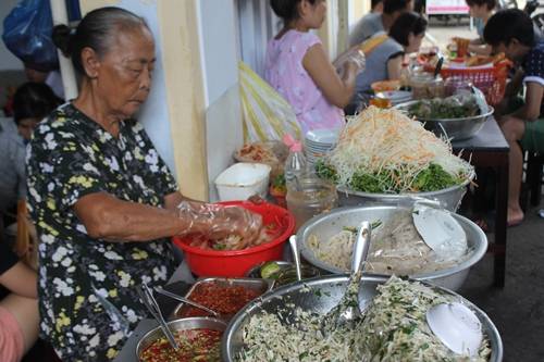 Mít trộn bà già Bà cụ 76 tuổi nhanh tay trộn mít cho hàng dài khách chờ là hình ảnh quen thuộc trong hẻm Lý Thái Tổ với người dân và du khách. Các khâu từ đi chợ chọn nguyên liệu, trộn mít, nêm gia vị… đều do chính tay bà làm, con cái trong nhà phụ giúp bưng bê cho khách. Bà chia sẻ, mít trộn da heo là món ăn vặt bình dân nhưng cần cầu kỳ trong từng khâu, thì mới có được độ ngon và được phục vụ suốt 30 năm qua. Ngay từ khâu luộc, mít cần giữ cho vừa dai vừa ngọt, tuyệt đối không để bị chát. Da heo cũng phải chọn loại da không quá mềm không quá dai. Các nguyên liệu khác như đu đủ, ớt, rau thơm... cũng được mua hàng ngày để đảm bảo độ tươi ngon. Ảnh: Cẩm Duyên.