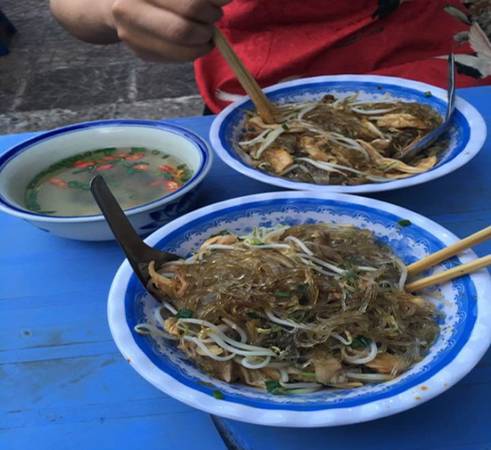 Miến trộn gà bao gồm miến, thịt gà xé nhỏ, rau thơm, lạc rang, nước sốt,… cho vào bát, trộn đều lên - món ngon từ gà Hà Nội. Thịt gà được lựa chọn khéo léo nên ngọt và mềm tự nhiên. Nước sốt chua ngọt hòa quyện với những sợi miến to, dai tạo thành một món mềm ngậy mà không gây ngán. Ngoài ra, bạn cũng có thể lựa chọn miến gà nước để thưởng thức. Miến trộn gà bán nhiều ở phố Gia Ngư, Hàng Hòm, giá một bát là 30.000 đồng. Ảnh: Dương Đình Quảng.