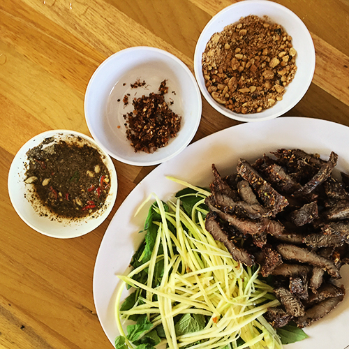 Bò khô muối kiến  Bò khô chấm cùng muối kiến là món ăn kích thích sự tò mò của nhiều khách phương xa. Thịt được thái thành từng miếng to cỡ bằng bàn tay rồi tẩm ướp gia vị đem nướng. Chủ quán khéo léo để thịt không quá cháy, vẫn giữ được độ ngọt, dai và không bị khô. Món ăn này sẽ tròn vị nếu bạn chấm cùng với muối được chế biến từ loại kiến vàng sống trên cây rừng hay ở các vườn.  Độ thơm, ngọt của thịt bò quyện cùng vị chua đặc trưng của muối kiến khiến bạn muốn ăn mãi không thôi. Bạn có thể mua món ăn này về làm quà tặng bạn bè, người thân, giá một kg thịt bò khoảng 500.000 đồng.