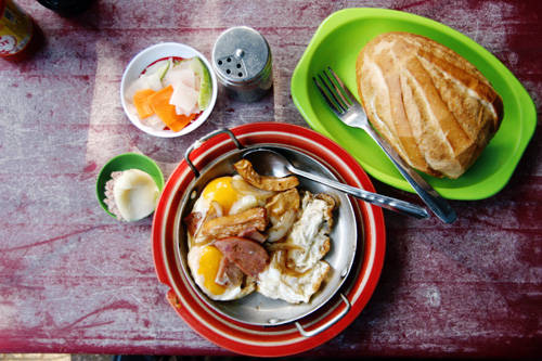 Đặc trưng của quán là món bánh mì chảo. Bên trong chảo là đủ thứ nguyên liệu như trứng gà ốp la, thịt nguội, xúc xích, chả cá, chả lụa... Tất cả đều được chiên nóng cháy cạnh cùng ít hành tây và dùng nóng với bánh mì. Nếu không thích dùng ốp la, bạn có thể gọi một phần thịt nguội thập cẩm riêng, rắc lên ít tiêu, nước tương, tương ớt. Giá trung bình một phần bánh mì ăn kèm trứng trên chảo là 40.000 - 45.000 đồng. Ảnh: Phong Vinh.