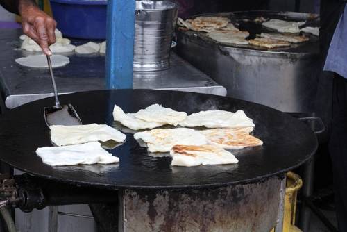 Roti Canai Roti Canai là bánh mì dẹt, du khách dễ thấy hàng bánh này ở Jalan Transfer, một khu phố ẩm thực của George Town. Món này thường ăn với cà ri như một bữa sáng. Quầy roti canai thường có hai đầu bếp, một người lấy bột nhào, người còn lại cho bột lên rán trên chảo lớn. Trông họ chế biến món ăn bạn sẽ liên tưởng tới những tay chơi trống thực thụ.