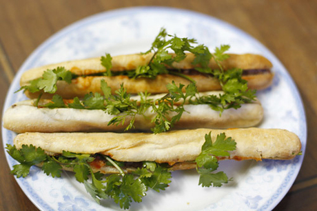 Bánh mì cay Hải Phòng  Du nhập lên Hà Nội cách đây khoảng chục năm, những chiếc bánh mì của đất cảng nhanh chóng trở thành món ăn quen thuộc của người dân Hà thành. Mỗi khi có khách tới mua, chủ hàng nướng lại những chiếc bánh nhỏ xíu, cho patê vào bên trong, thêm chút chí chương (tương ớt) giúp kích thích vị giác. Mỗi người có thể ăn 3-4 chiếc với giá khoảng 10.000 - 15.000 đồng. Bánh mì cay Hải Phòng thường không ăn với rau mùi, nhưng bạn có thể cho thêm nếu thích. Ảnh: Út Liên.