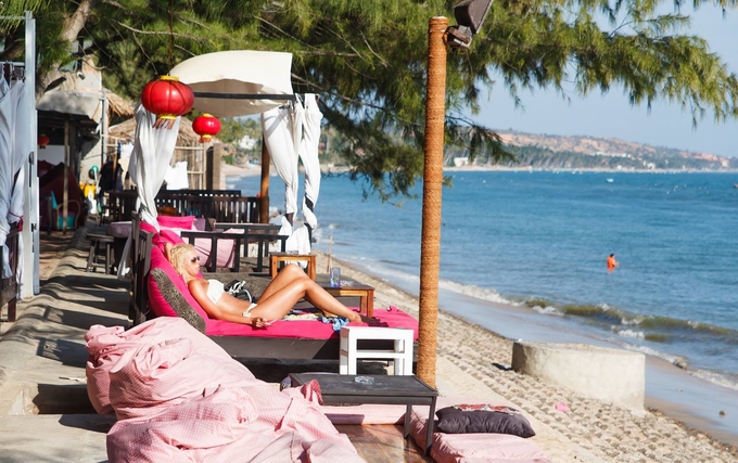 Du khách nằm trên ghế dài đọc sách, sưởi nắng sau khi tắm biển tại Dragon Beach Bar Mũi Né