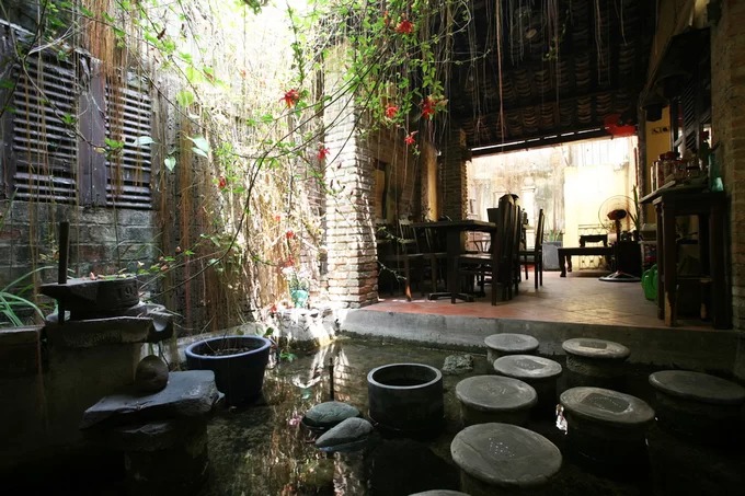 Phía sau gian nhà bên trái quán cà phê nhà cổ The Home có một khoảng sân trời, nối liền với không gian cà phê phía sau. Để đi tới chỗ này phải bước trên những bậc đá trên mặt nước.