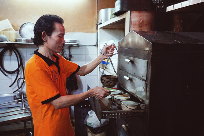 Một nhân viên gắp thố gà tiềm sau khi đã hâm nóng.