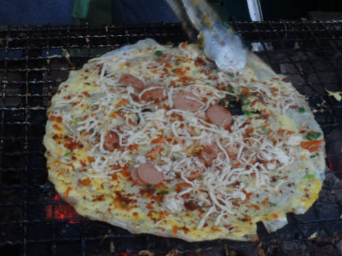Các nguyên liệu như tôm khô, bột phô mai, xá xíu, xúc xích, gà xé phay, thịt bò khô, rau thơm được rắc trên mặt bánh