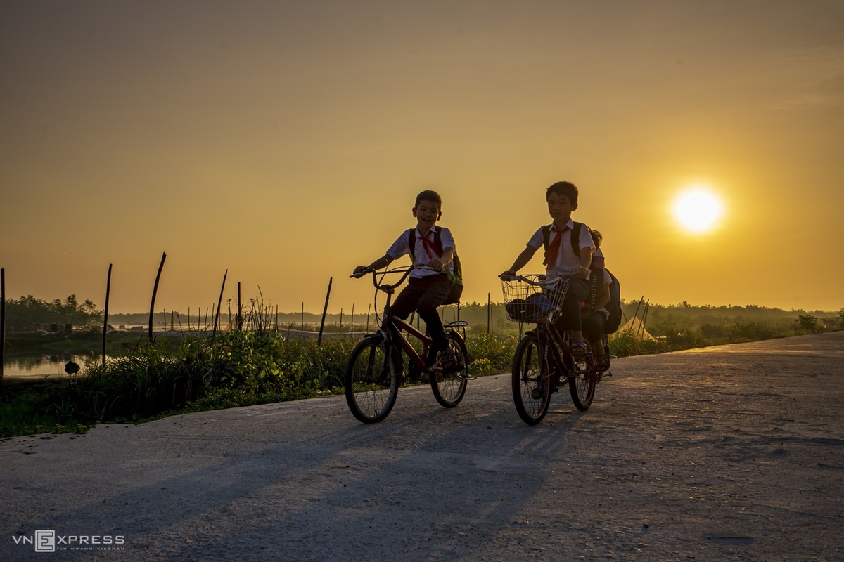 Trẻ em đạp xe đi học lúc bình minh trên đường bê tông cạnh đầm Quảng Lợi mang đến bức tranh quê hương thanh bình.